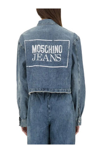 Back view of moschino jeans women’s blue denim cropped jacket with white embroidered logo on back