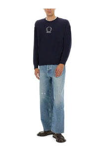 Navy blue knit sweater with white embroidered laurel wreath emblem paired with moschino men’s cotton denim jeans blue