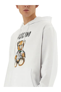 Moschino men’s white teddy print hoodie featuring a cartoon teddy bear graphic with a red and green bow tie
