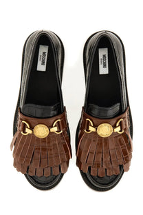 Brown fringed leather slip-on sandals with gold tone coin and buckle accents and a black croc embossed sole by moschino