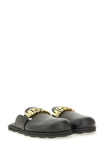 Moschino women’s sabot black leather slide sandals with bold gold-tone Moschino logo across the front