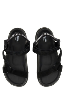Moschino women’s black strap sandals with suede look and glossy black rubber sole featuring white logo on footbed