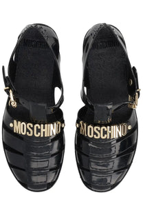Moschino women’s black glossy patent leather sandals with gold-tone Moschino lettering across the front