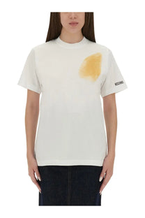 Moschino women’s white t-shirt featuring a yellow stain graphic on the chest and black branding on the sleeve