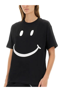 Moschino women’s black short-sleeved cotton t-shirt featuring a large white smiley face graphic on the front