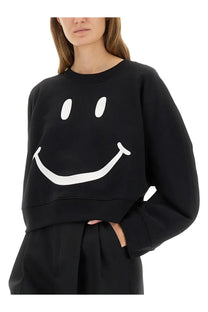 Moschino women’s black cropped sweatshirt with large white smiley face graphic on front made from soft fabric