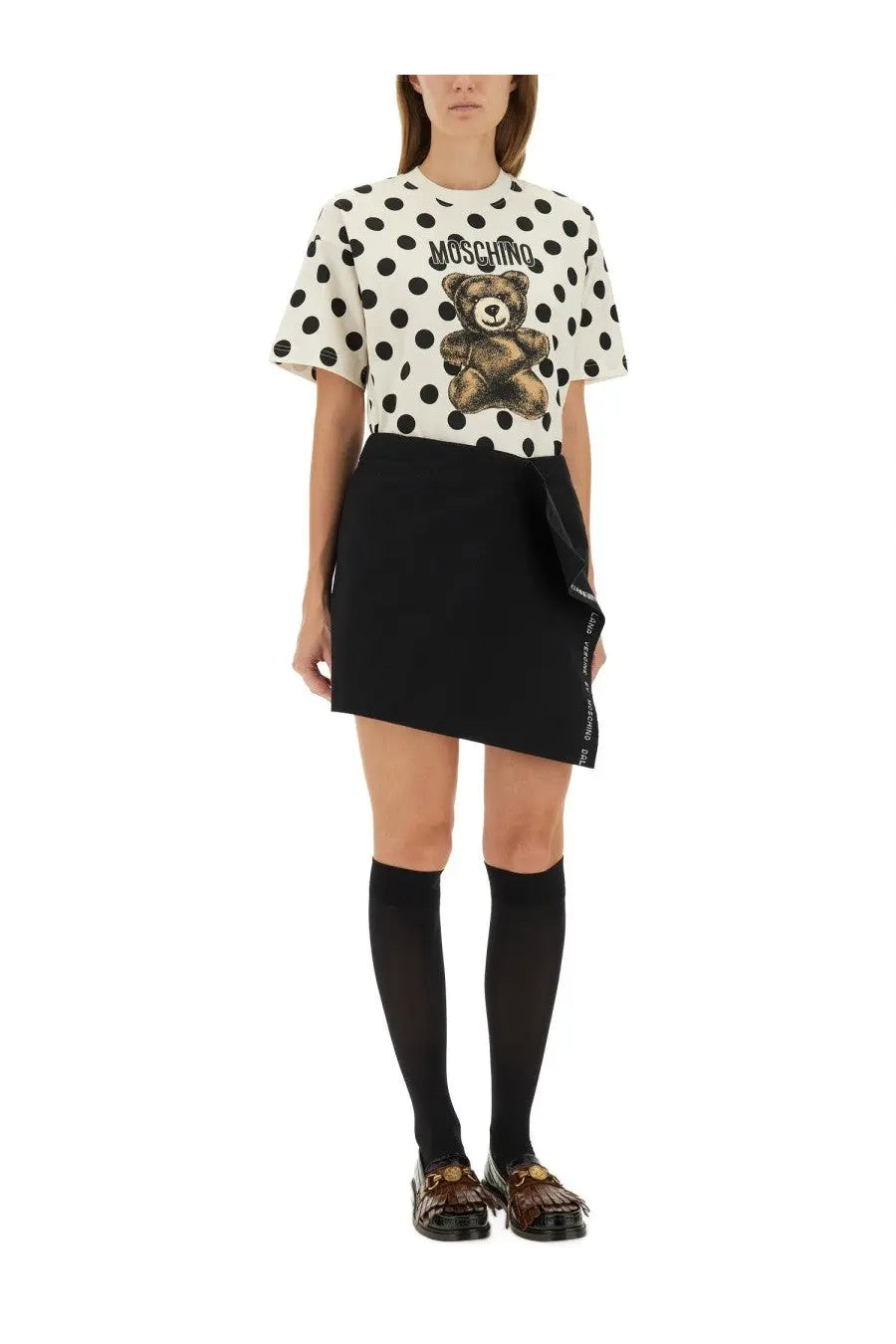 White polka dot moschino t-shirt with brown teddy bear graphic and logo above paired with black wool wrap skirt