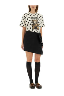 White polka dot moschino t-shirt with brown teddy bear graphic and logo above paired with black wool wrap skirt