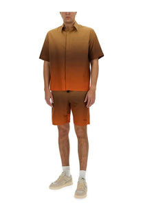 A man wearing MSGM men’s cotton Bermuda shorts and a matching short-sleeved button-up shirt in orange to brown gradient