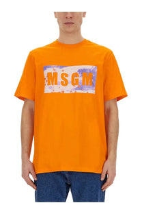 Bright orange MSGM men’s t-shirt with a bold rectangular graphic and splattered purple and white paint accents
