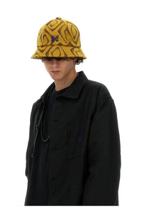 Needles men’s yellow bucket hat with brown abstract swirl pattern and small purple butterfly emblem