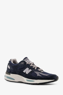 New balance men’s suede low top sneakers in navy blue with mesh, gray laces, silver logo, and teal air cushioning units