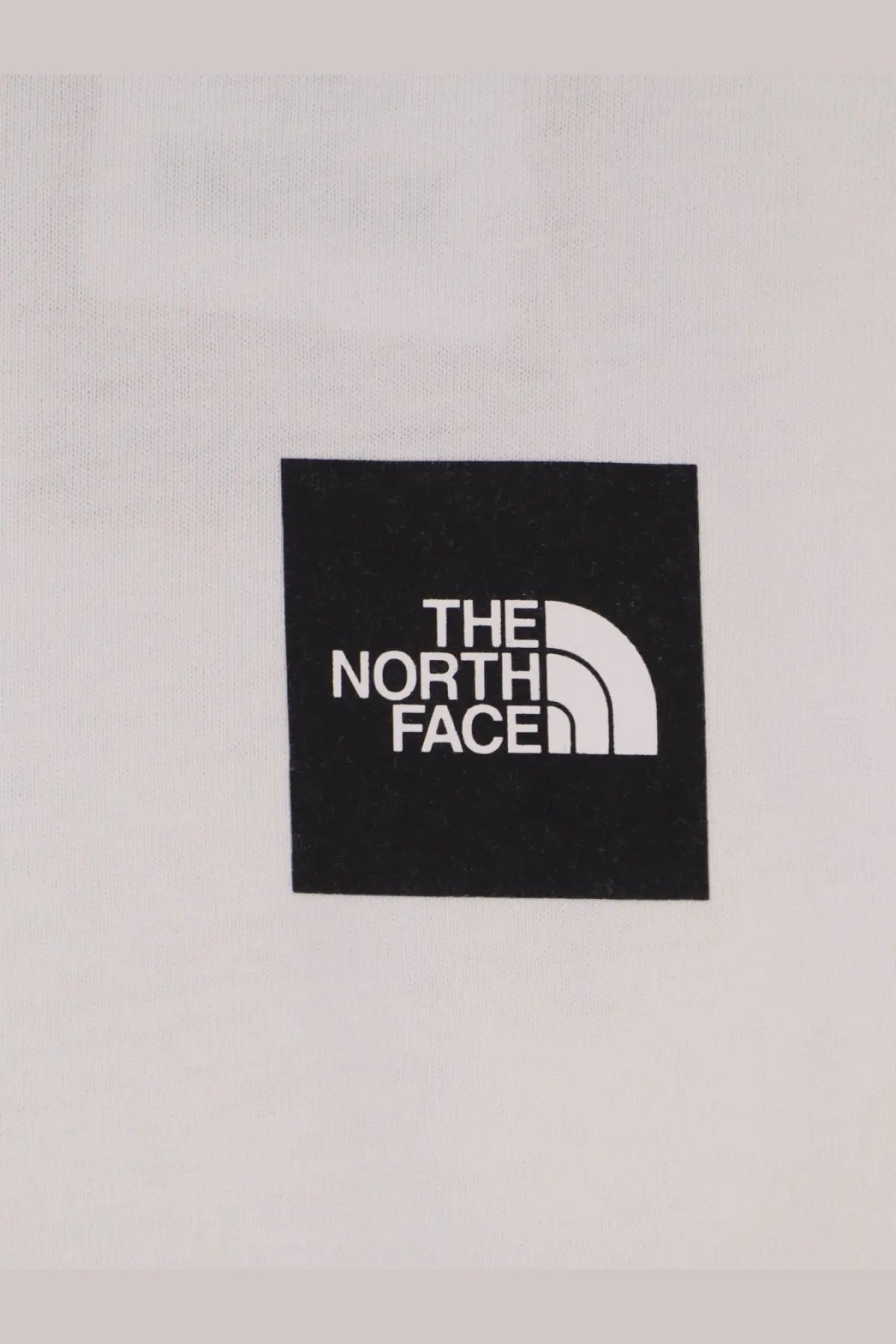 Black square patch with white the north face logo and half dome symbol on the north face mens white cotton shirt