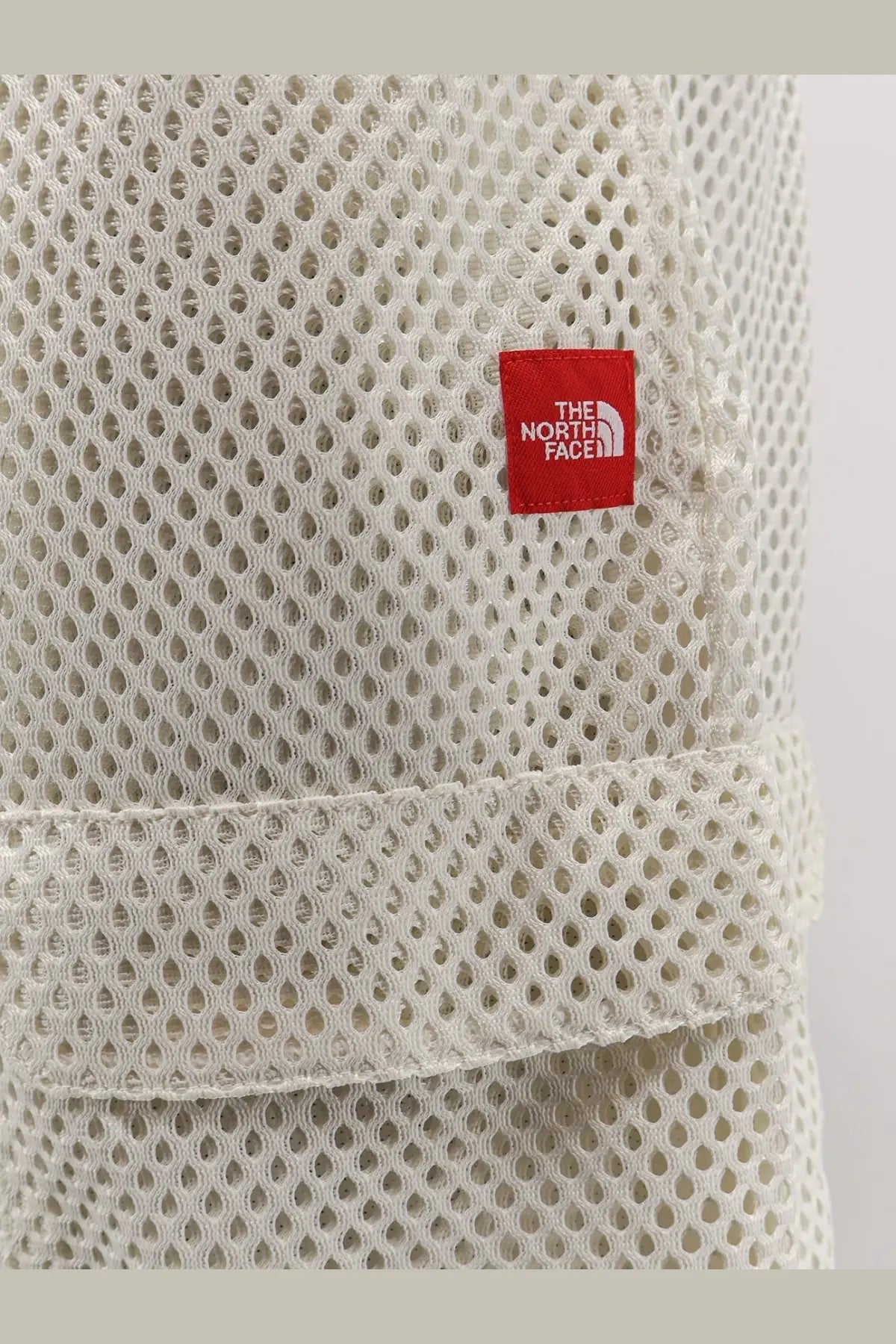 Off-white mesh fabric hat with a red the north face logo patch paired with men’s nylon bermuda shorts white