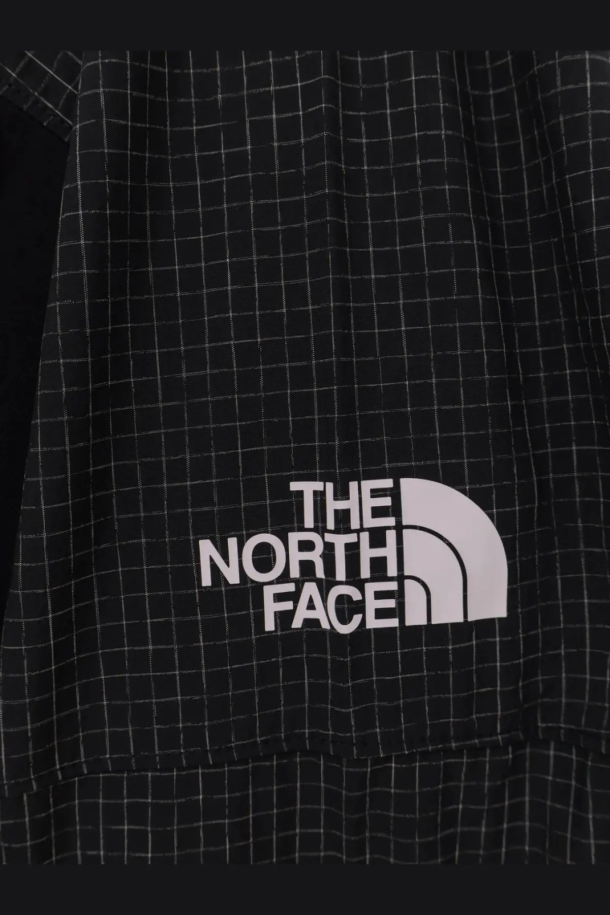 The north face men’s relaxed fit jacket in black features a black and white grid pattern with a white logo patch