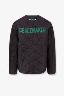 Back view of oamc peacemaker men’s black quilted compact liner jacket with green embroidered peacemaker lettering