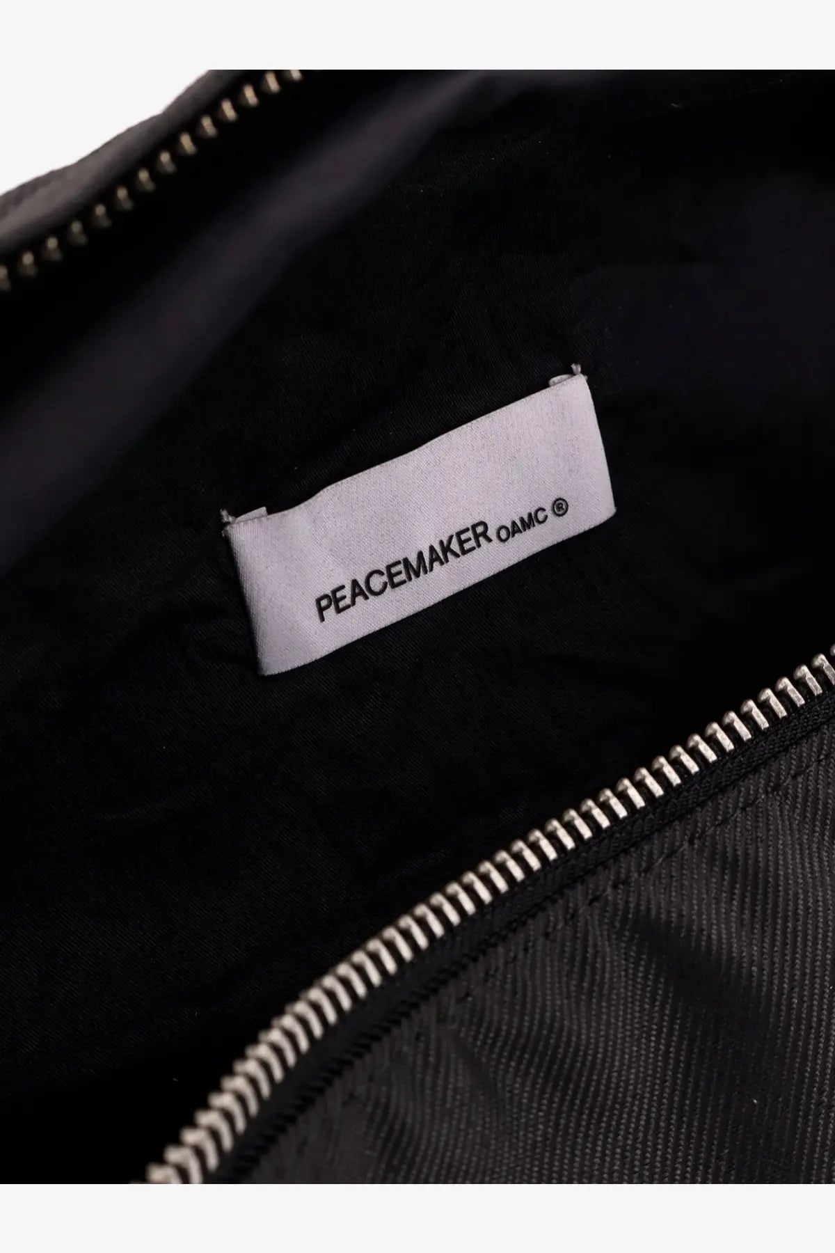 Black interior label with peacemaker oamc text on white background inside oamc peacemaker men’s military nylon belt bag black