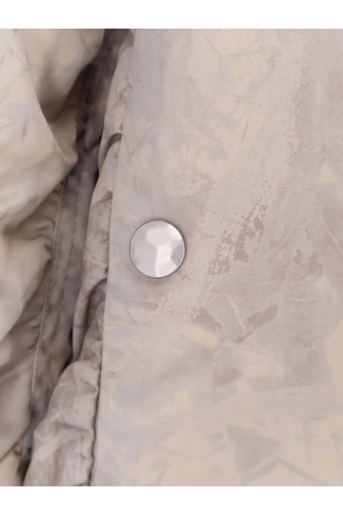 A round faceted silver button with metallic sheen on light gray fabric of oamc peacemaker men’s green bomber jacket