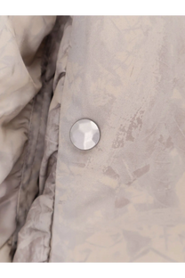 A round faceted silver button with metallic sheen on light gray fabric of oamc peacemaker men’s green bomber jacket
