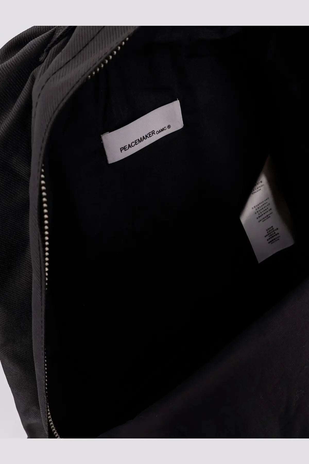 Black oamc peacemaker men’s nylon backpack interior showing white brand label and durable fabric lining