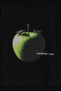 A glossy green apple with two wasps perched on it displayed alongside the oamc peacemaker men’s black shirt