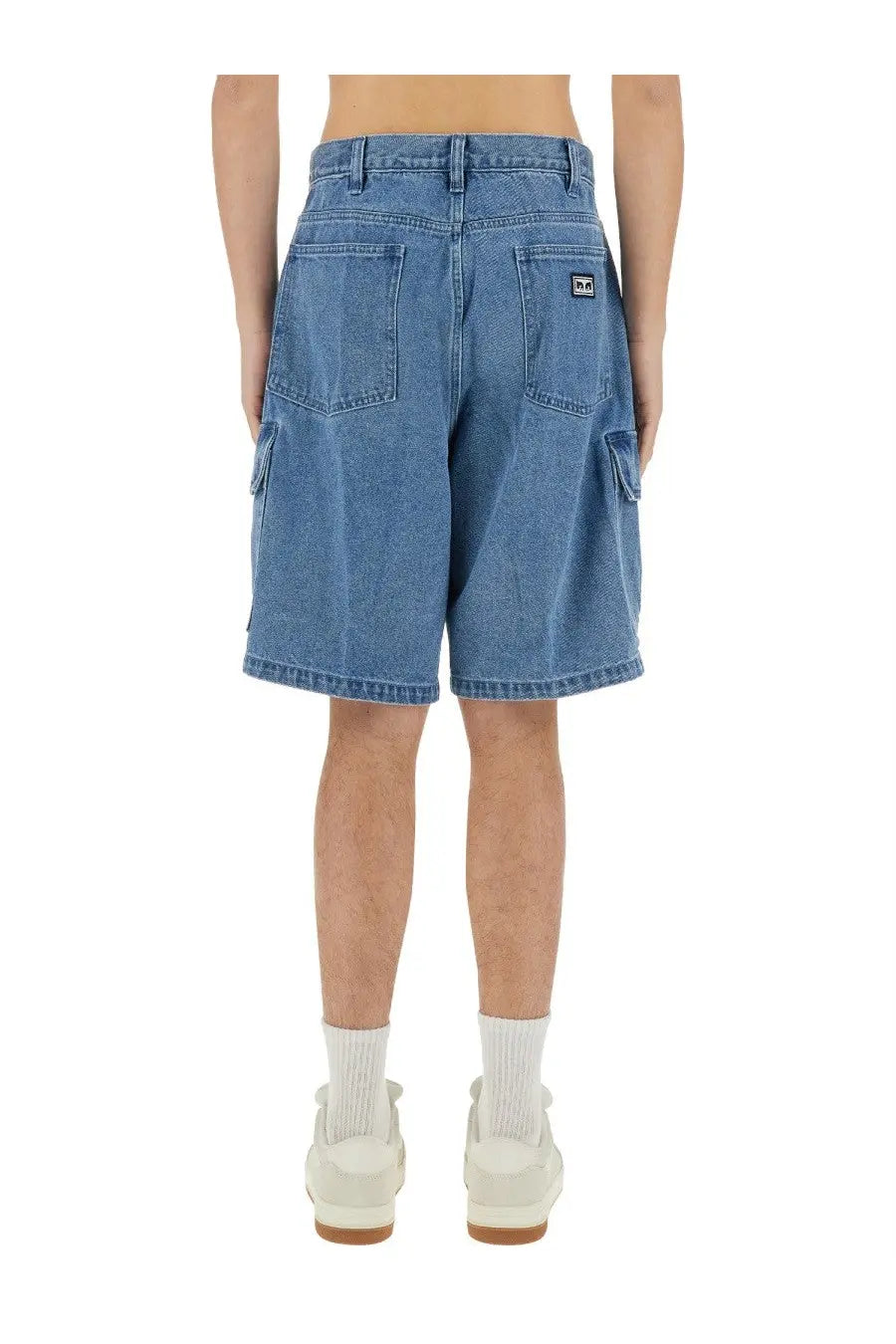 Back view of obey men’s baggy bigwig blue denim cargo shorts with pockets and brand logo on the right pocket