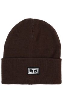 Brown knit beanie with black and white rectangular logo patch featuring stylized eyes from obey men’s cap brown collection