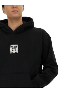 Obey men’s icon hoodie black features a black cotton fabric with a white embroidered face logo on the chest