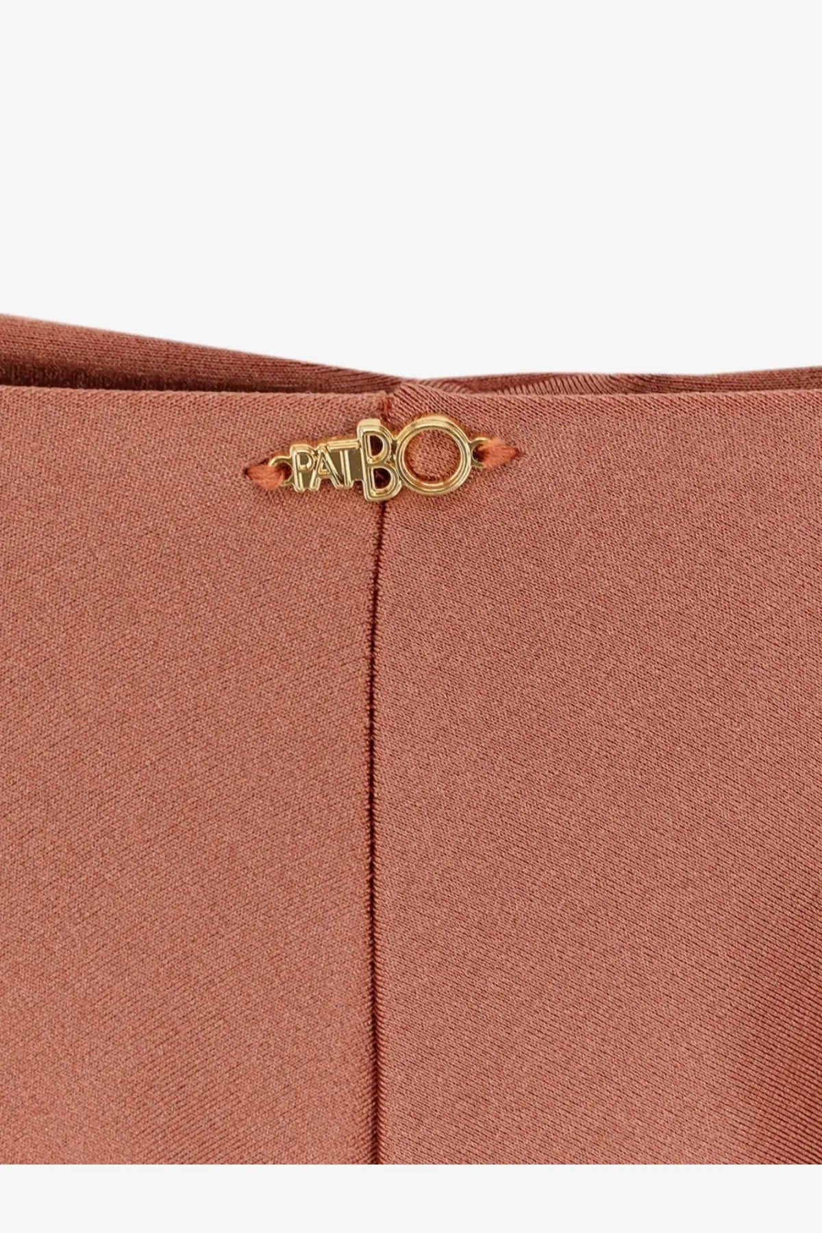 A gold-tone metal patbo logo plaque on rust-colored lycra fabric of patbo women’s orange bikini bottoms