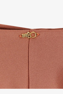 A gold-tone metal patbo logo plaque on rust-colored lycra fabric of patbo women’s orange bikini bottoms
