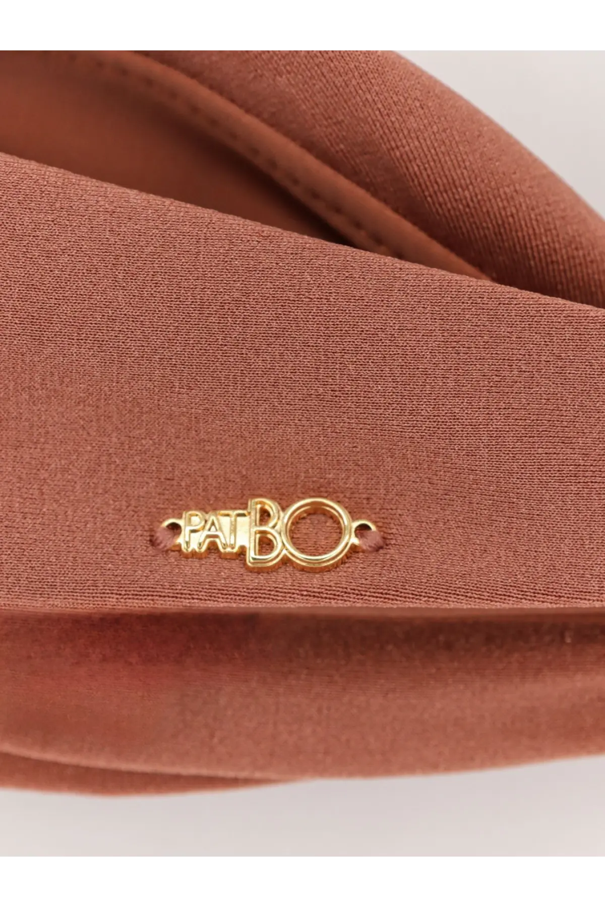 A tan leather crossbody bag with a gold tone patti bo logo plaque shown with patbo women’s orange lycra bikini top