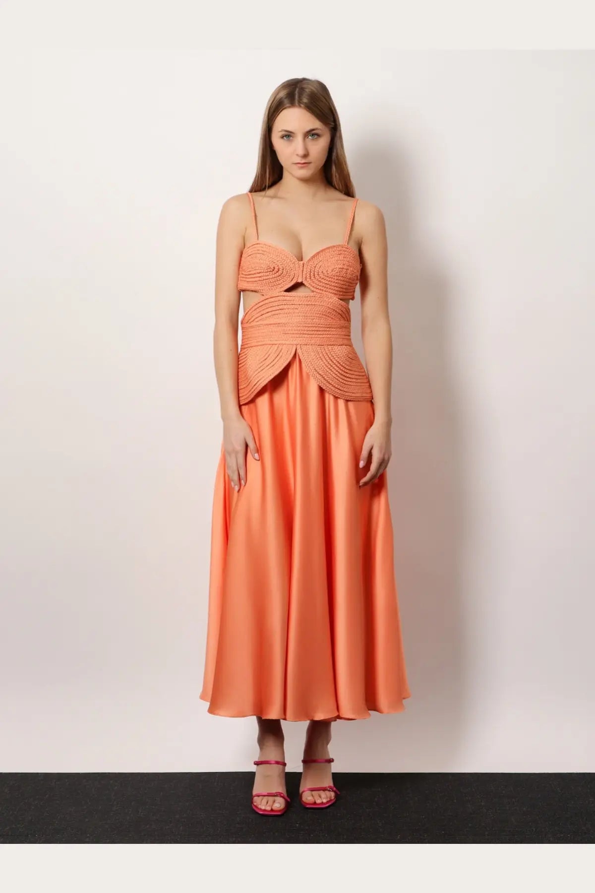 A woman wearing a coral patbo women’s satin sunset midi dress with a woven bodice and flowing satin skirt