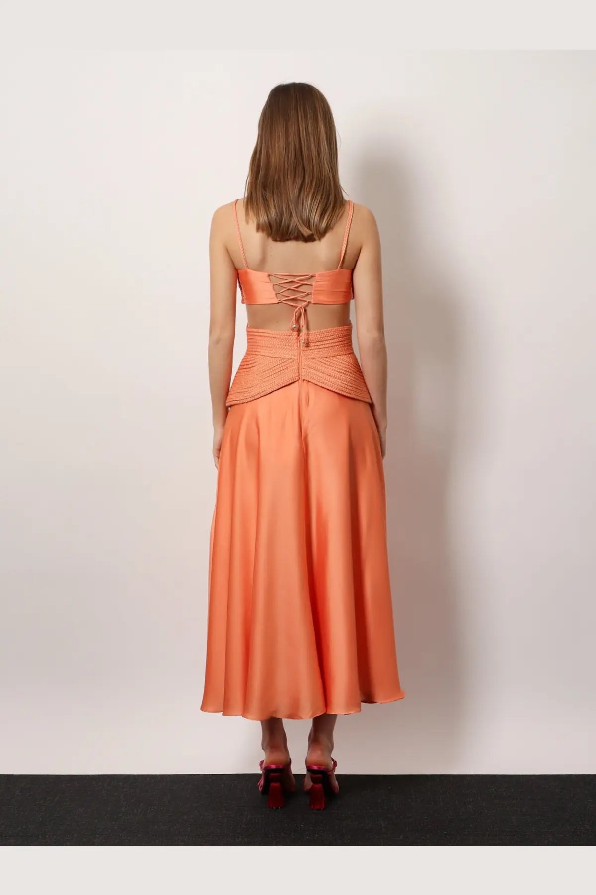 A woman wears patbo women’s satin sunset midi dress back view in orange two-piece satin with lace-up back top and flowing skirt