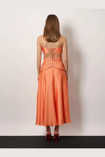 A woman wears patbo women’s satin sunset midi dress back view in orange two-piece satin with lace-up back top and flowing skirt