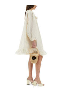 A woven wicker basket with rounded handle and black circular detail shown with patou womens white ruffle hem dress