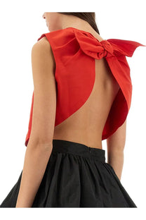 A vibrant red satin Patou women’s top with a large bow at the back paired with a black skirt showing the back view