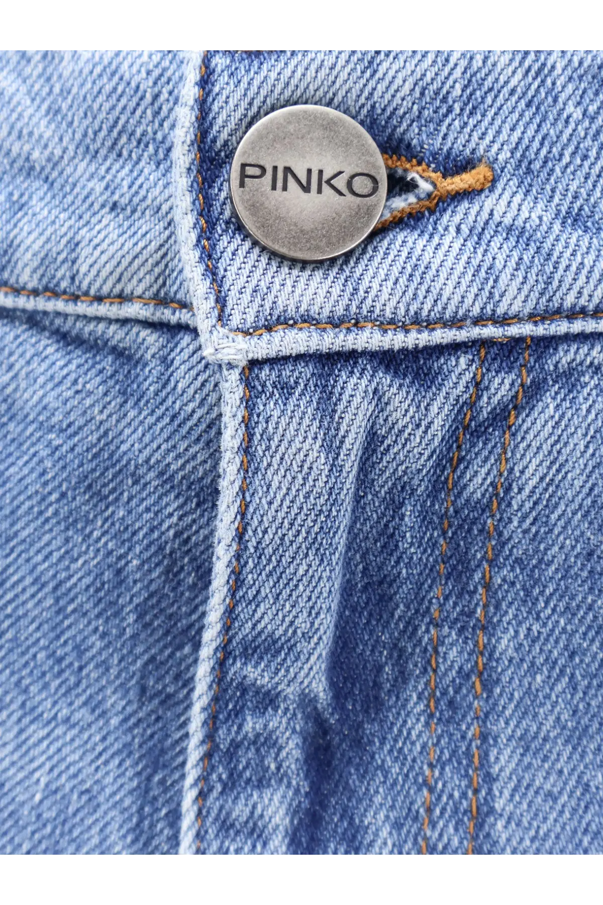 A silver circular button engraved with pinko on light blue denim fabric of pinko womens blue denim jeans bronze