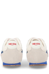 Cream-colored suede pro-keds men’s reacer sneaker with blue rubber soles and red branding on the heel tab back side