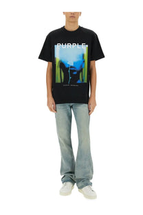 Black short-sleeved t-shirt with a bold purple graphic and abstract blue green face paired with purple brand coated flare jeans blue