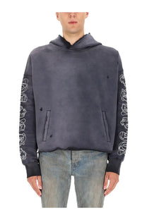 Dark gray purple brand men’s hoodie with white embroidered skull sleeves and distressed frayed hem visible from front