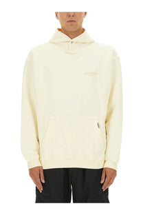 Cream-colored Represent men’s hoodie beige with hood, subtle embroidered logo, and front pocket with small zipper pull