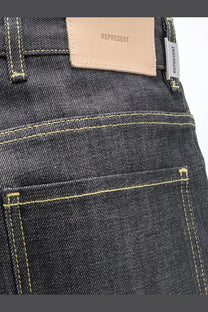 Represent men’s selvedge denim shirt black styled with dark-wash denim jeans featuring yellow stitching and beige leather patch