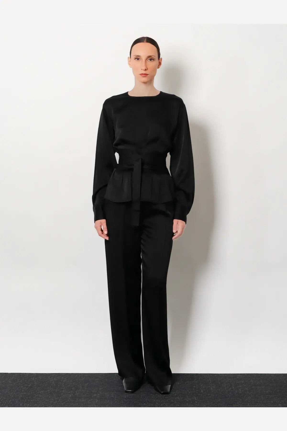 Black satin peplum top with long sleeves and tied waistband paired with rohe womens relaxed satin trousers black
