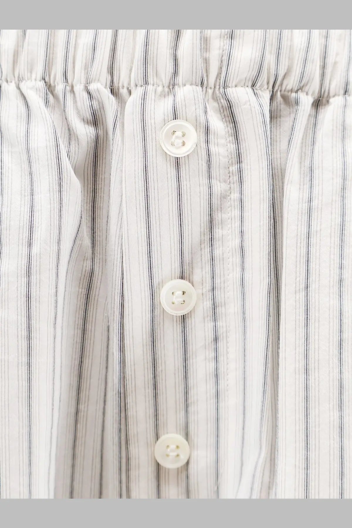 White buttons with subtle sheen on rohe womens silk trousers featuring fine vertical light gray and white stripes fabric