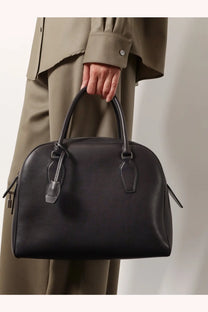 The row women’s india leather handbag is a black structured leather satchel with top handles for stylish carrying