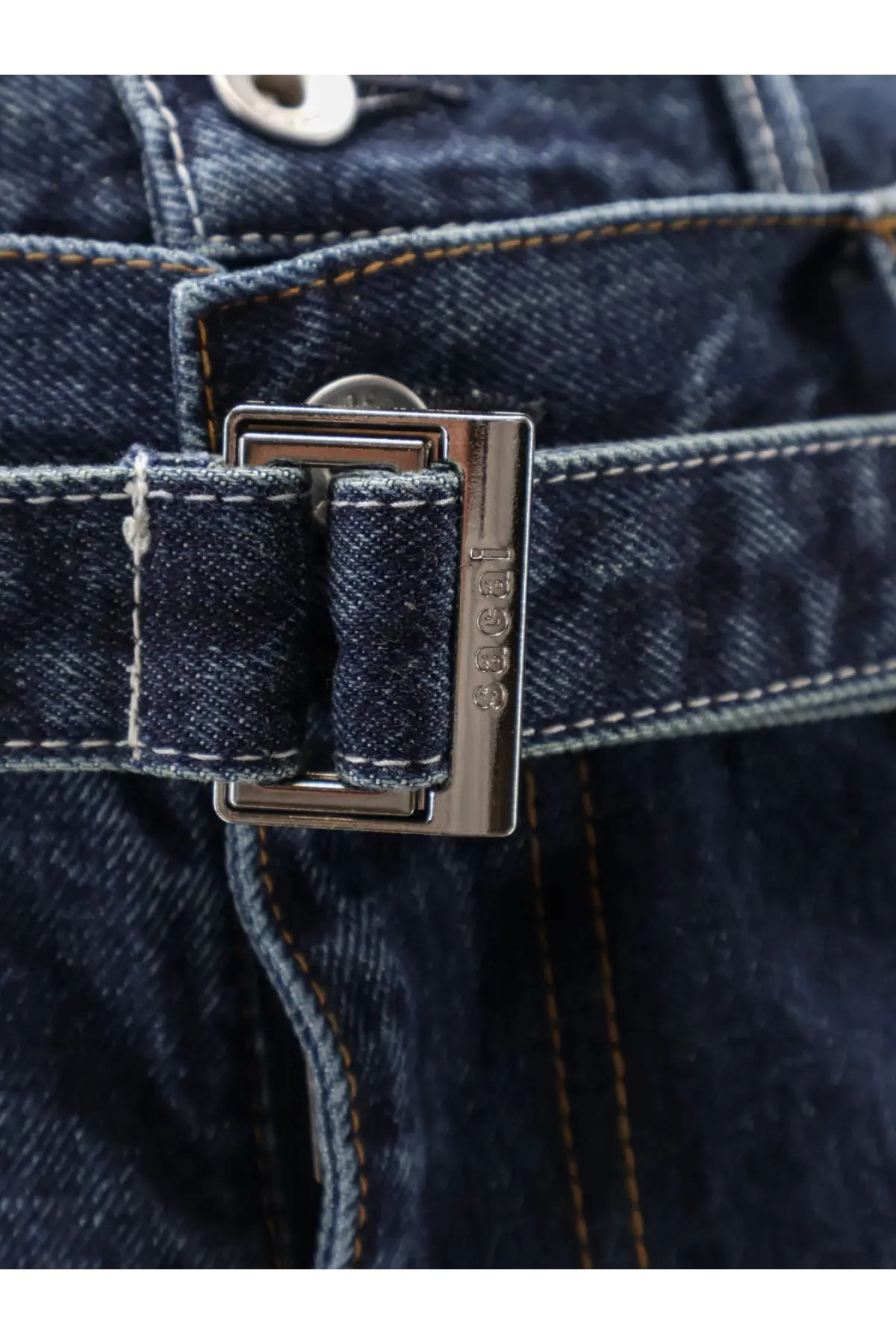 Sacai men’s blue denim jeans with silver-toned rectangular buckle embossed 1982 on dark indigo denim fabric