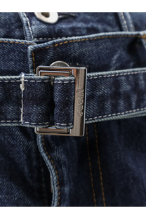 Sacai men’s blue denim jeans with silver-toned rectangular buckle embossed 1982 on dark indigo denim fabric