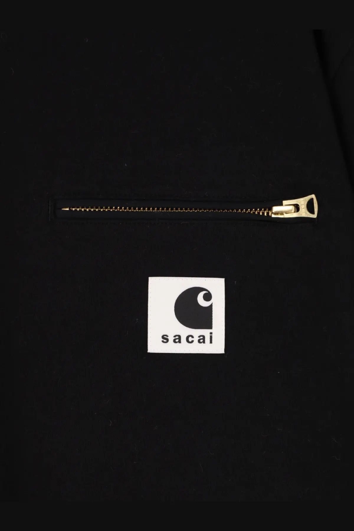 Black carhartt x sacai collaboration jacket with gold zipper and white square logo patch on front in cotton material