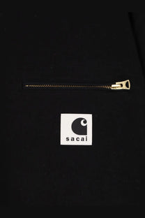 Black carhartt x sacai collaboration jacket with gold zipper and white square logo patch on front in cotton material