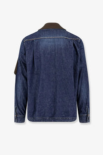 Sacai men’s blue denim jacket with dark blue fabric, contrasting brown collar, and brown sleeve patch